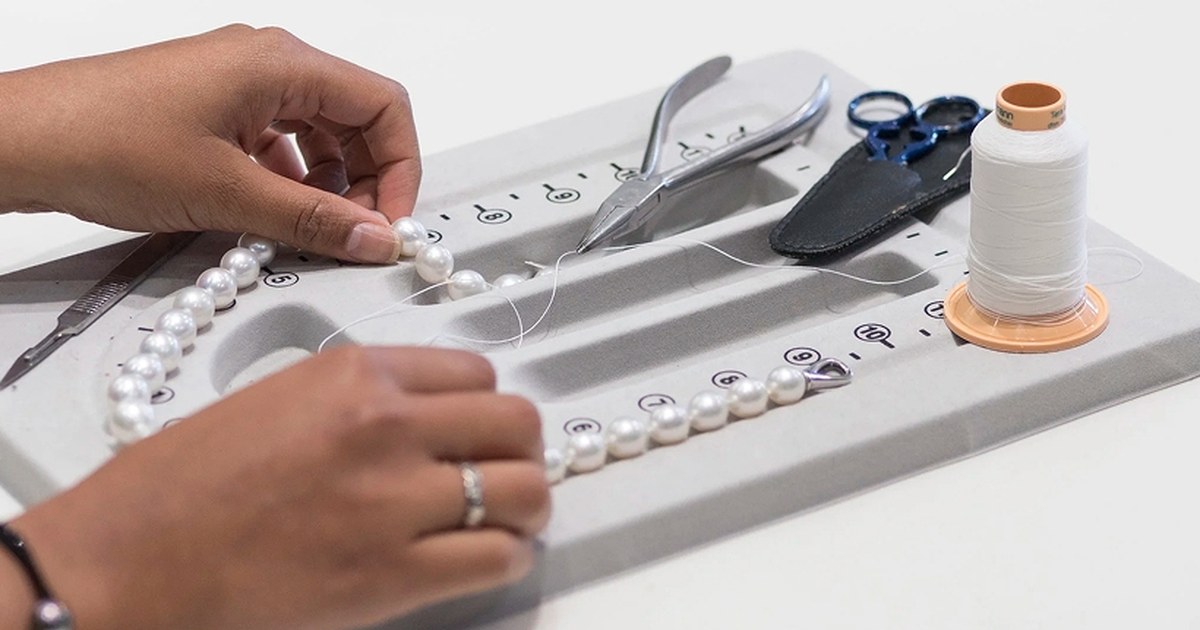 Hands knotting a strand of white pearls on a jeweller's board at Scagnetti Fine Jewellers